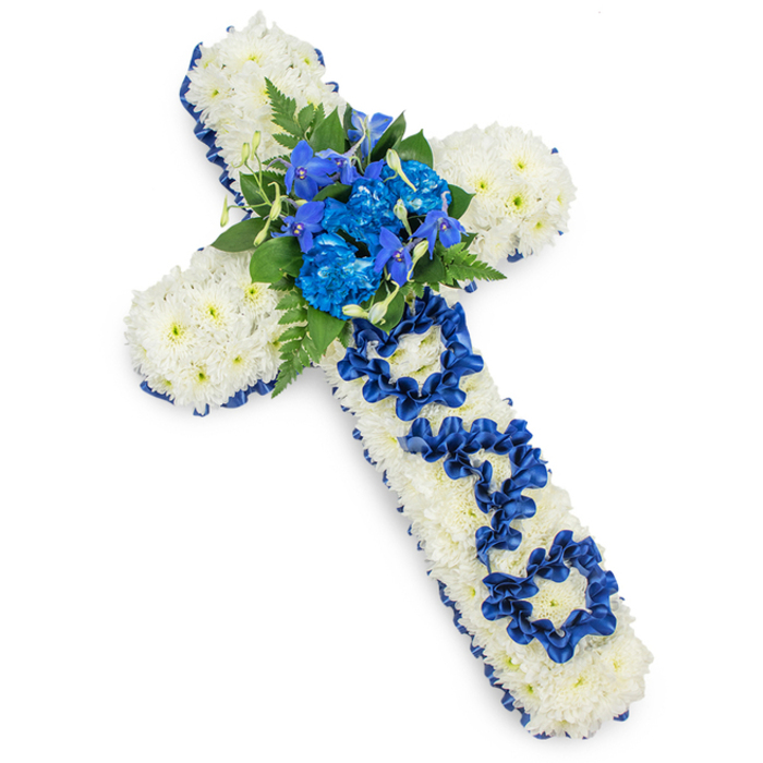 A thoughtfully designed floral cross sits against a spotless white background, its strong yet gentle presence evoking faith, remembrance, and familial love. The cross is entirely composed of small white spray chrysanthemums, each blossom placed closely to the next so that the surface appears thick, plush, and flawlessly even, without gaps or exposed stems. This soft floral cushion is crisply edged with a royal blue satin ribbon, which traces the perimeter of the arms and vertical stem in a continuous, gleaming border, giving the arrangement a refined, almost embroidered look. At the very centre of the cross, a lavish spray of royal blue flowers becomes the main focal point. Here, rich blue carnations with frilled, overlapping petals cluster together, joined by taller, more delicate spikes of blue flowers reminiscent of delphiniums or orchids, which lift the eye upward. Nestled among them are dark green fern fronds and layered leaves, their deeper tones setting off the blues and whites and adding a subtle sense of depth and movement. Running down the vertical bar, the word DAD is carefully created using the same blue ribbon, shaped into clear, rounded letters that are tucked into the chrysanthemum cushion, making the tribute both visually striking and deeply personal. The even white background and soft shadow beneath the design help to highlight the cross's three-dimensional structure, suggesting a substantial, professionally made piece, perhaps destined for a farewell gathering in Leyton, near local landmarks such as Leyton Midland Road or the quiet residential streets surrounding it. The overall effect is one of peaceful respect and enduring affection, ideal for honouring a much-loved father at a funeral or memorial service.